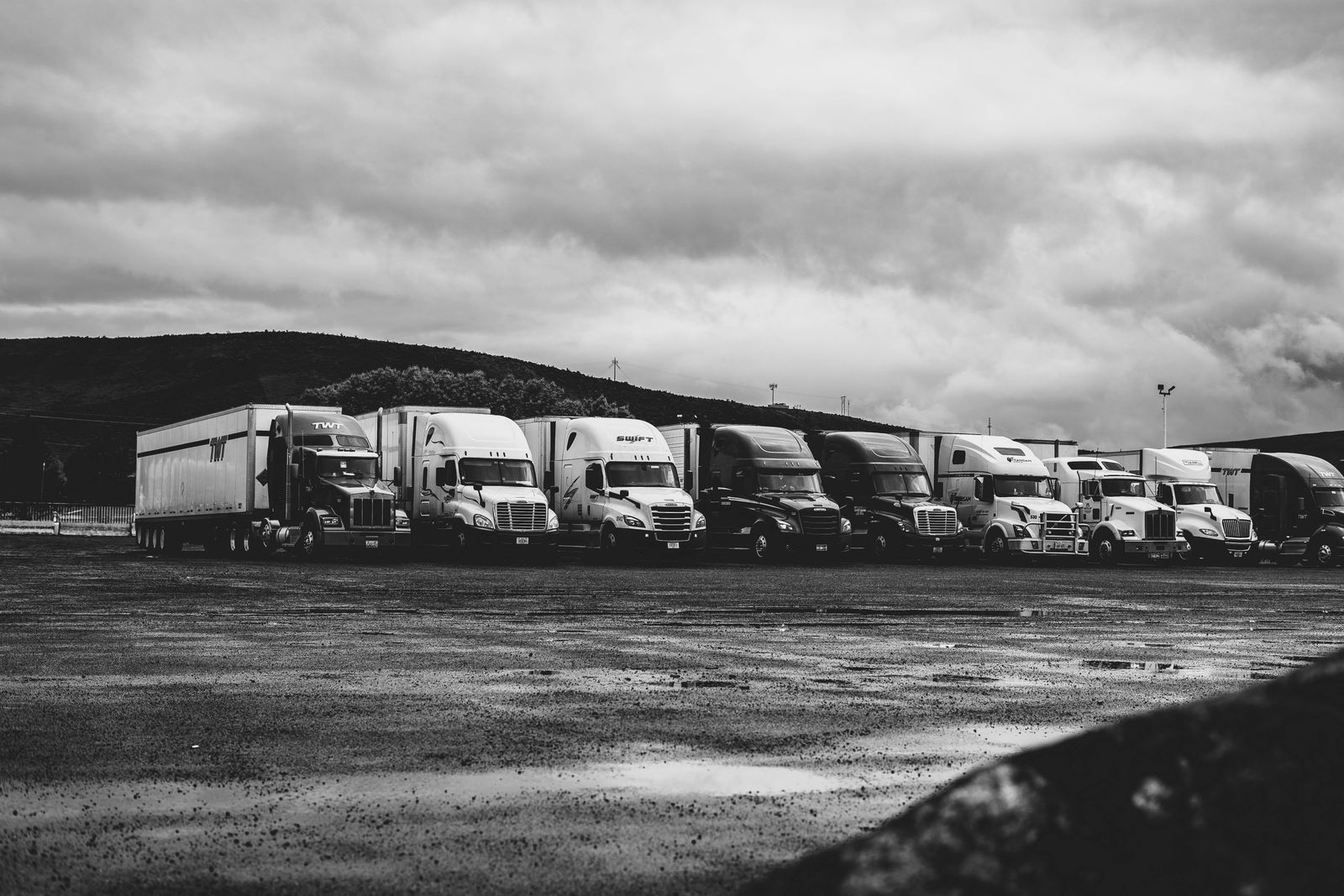 A row of parked semi trucks sitting idle in a lot under an overcast sky.