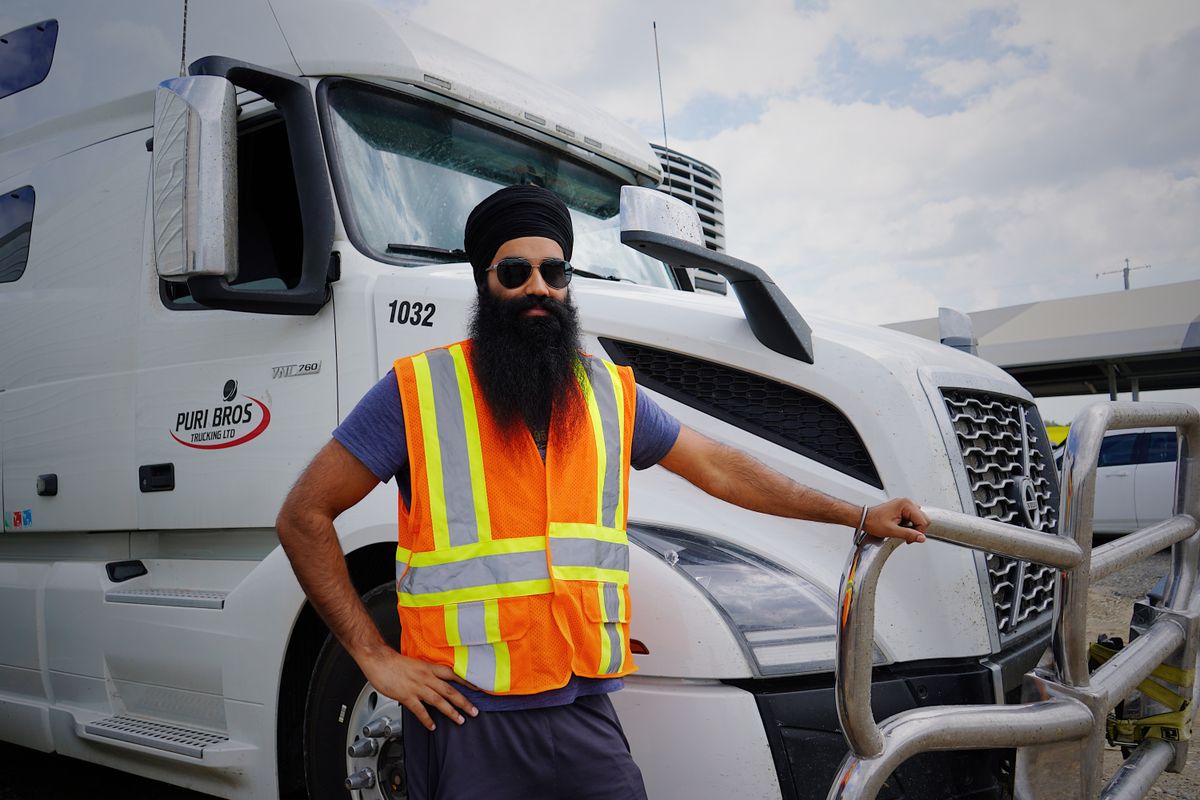 A commercial driver in a high visibility vest standing beside a tractor unit.